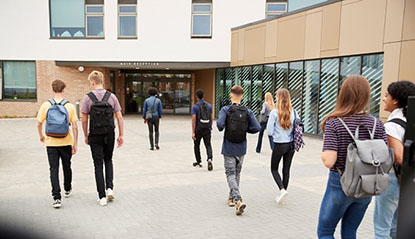 A group of teenage students walking toward the high school entrance.