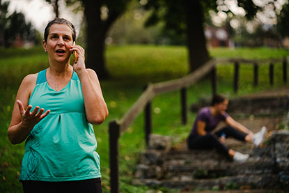 Woman on the phone calling for help while an injured runner sits on the ground behind her.