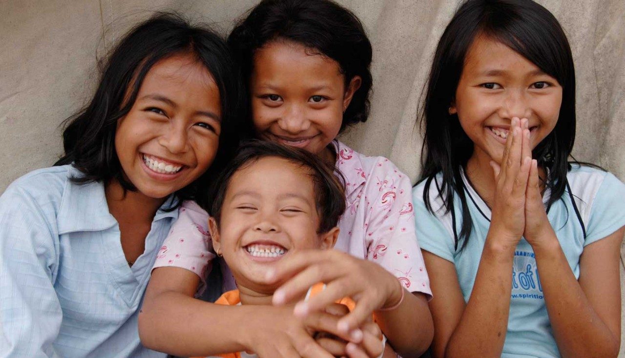 Children sitting in front of a tent share a laugh