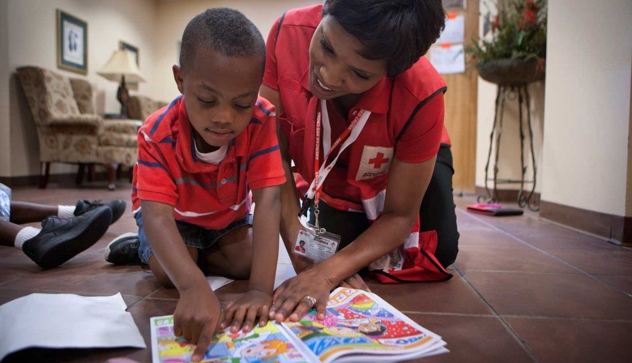 Female Red Cross volunteer helping young boy read a book