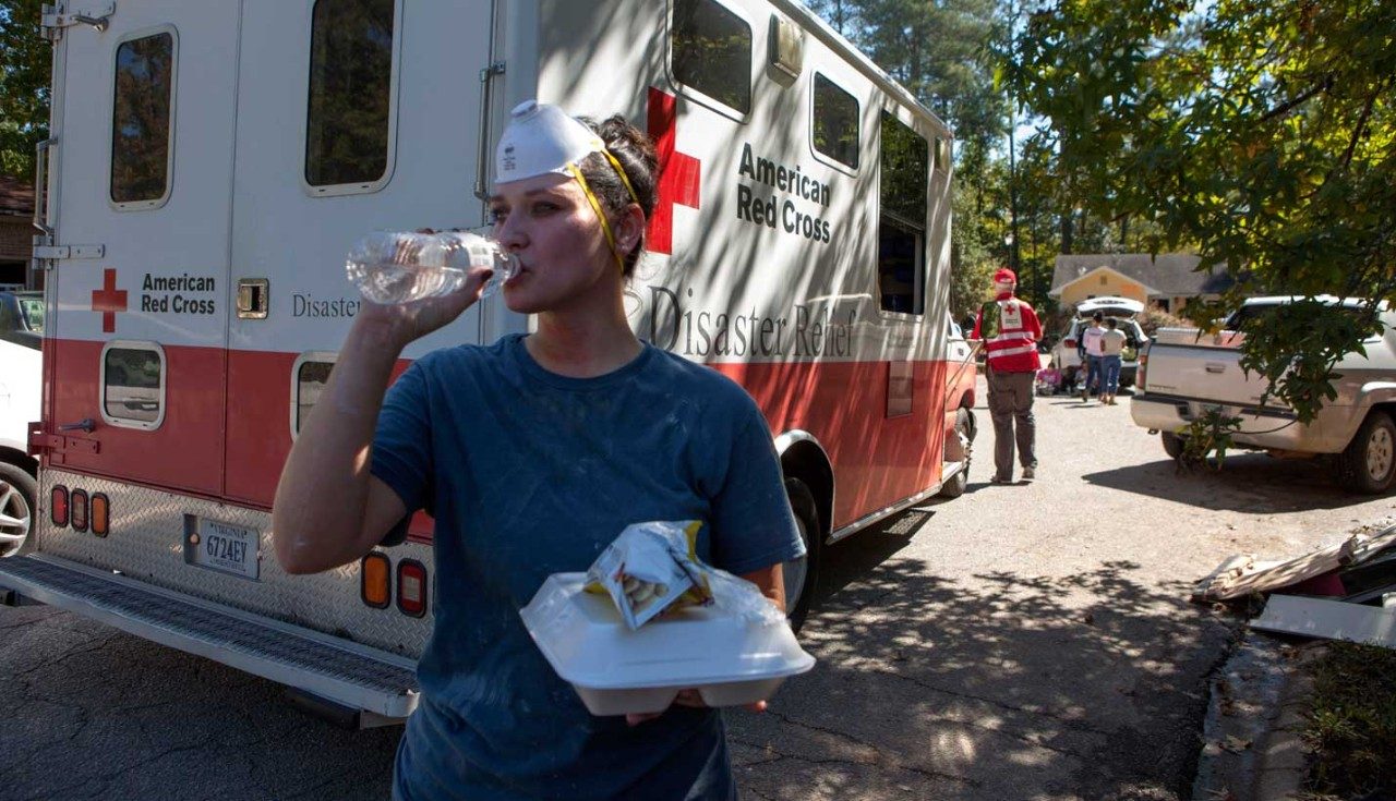 Young woman drinking water near Red Cross vehicle