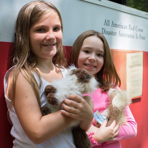 Smiling girls holding stuffed animals standing in front of an emergency response vehicle
