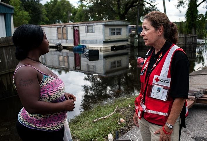 Red Cross volunteer speaking with woman near flooded mobile home