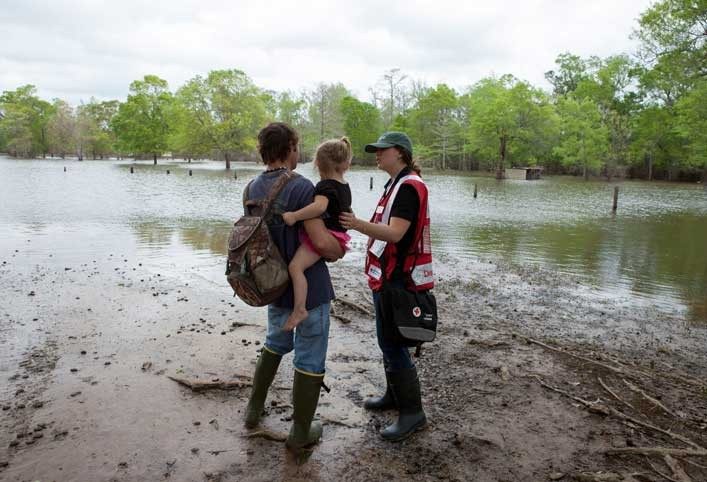 Red Cross volunteer speaking with family near flooded area