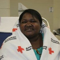 A woman in a shelter with a Red Cross blanket around her.