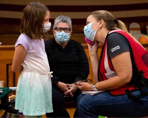 red cross volunteer talking to a young girl at a emergency shelter in their role supporting casework during a disaster response
