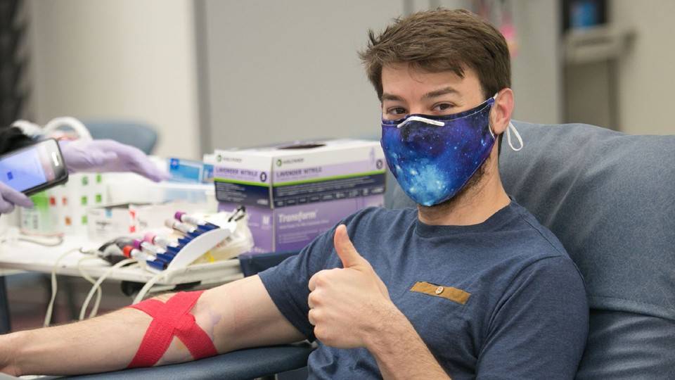 Person donating blood giving thumbs up with mask on