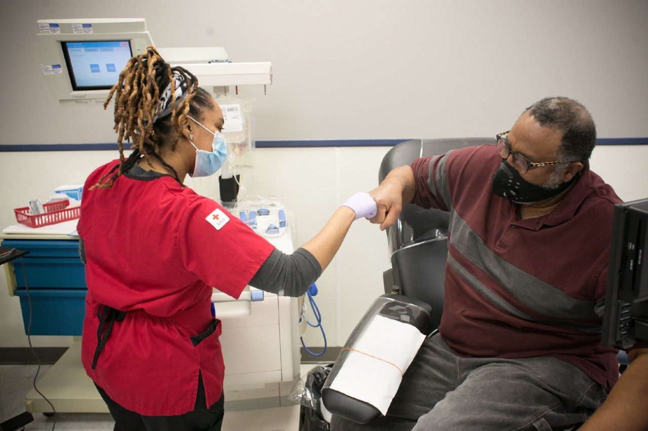 Red Cross nurse giving a fist bump to patient sitting in a chair.