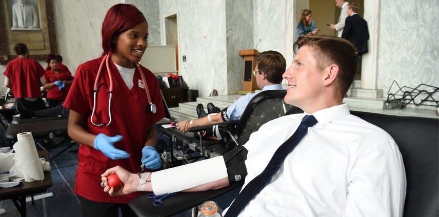 Man donating blood with Red Cross nurse next to him.