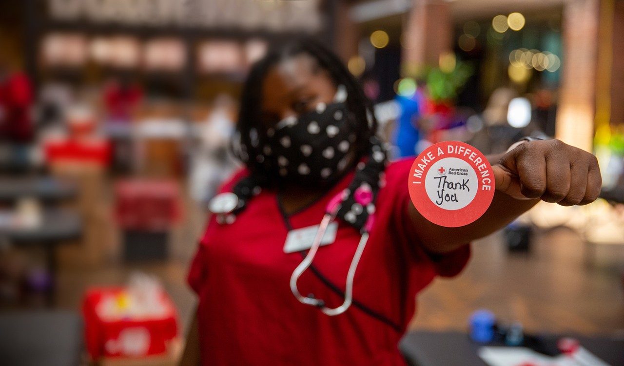 Red Cross nurse wearing mask and stethoscope holding a Thank You sticker.