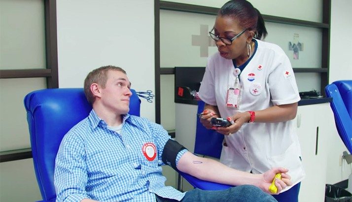 Man sitting in a chair giving blood and speaking with a phlebotomist