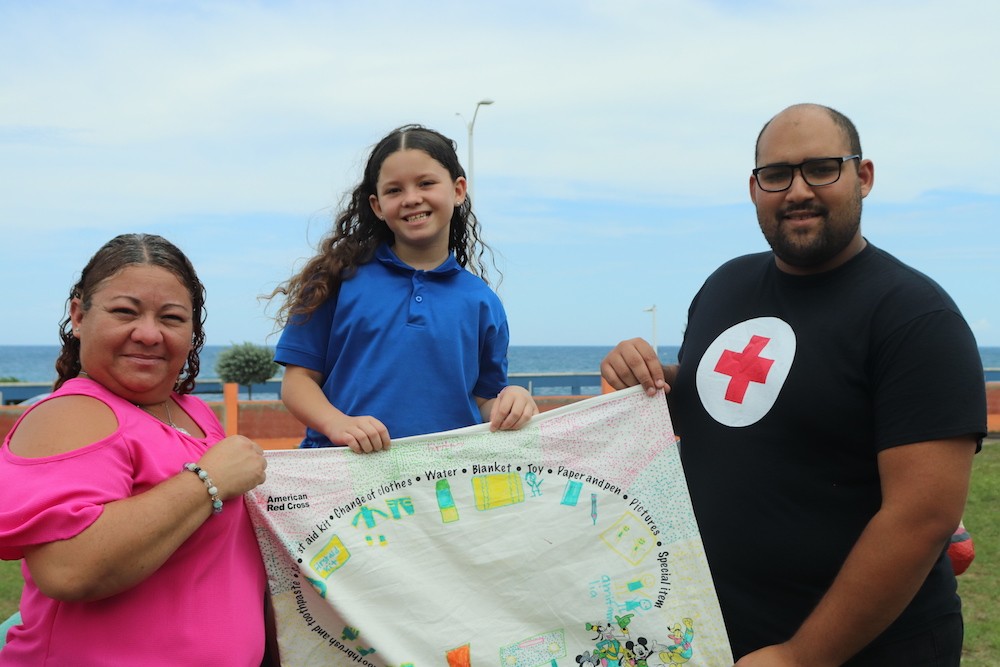 Fotografía de un voluntario de la Cruz Roja con Britney y su mamá Yessenia en el programa nacional "Mi Funda de Almohada".