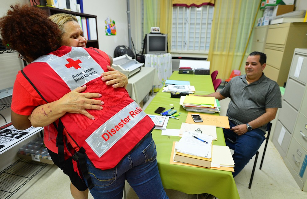 Fotografía de la directora Bianca Gonzalez de la Escuela Angelita Delgado Sella del municipio de Lares, recibiendo un abrazo de una voluntaria de la Cruz Roja, junto con Ramón Arroyo, maestro de educación especial, después de recibir paneles solares para la escuela.