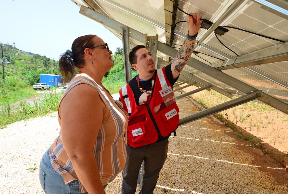 Fotografia de un voluntario de la Cruz Roja con una mujer, verificando la instalación de paneles solares,