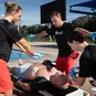 A group of lifeguards using an AED and rescue mask to resuscitate an unconscious person near a swimming pool.