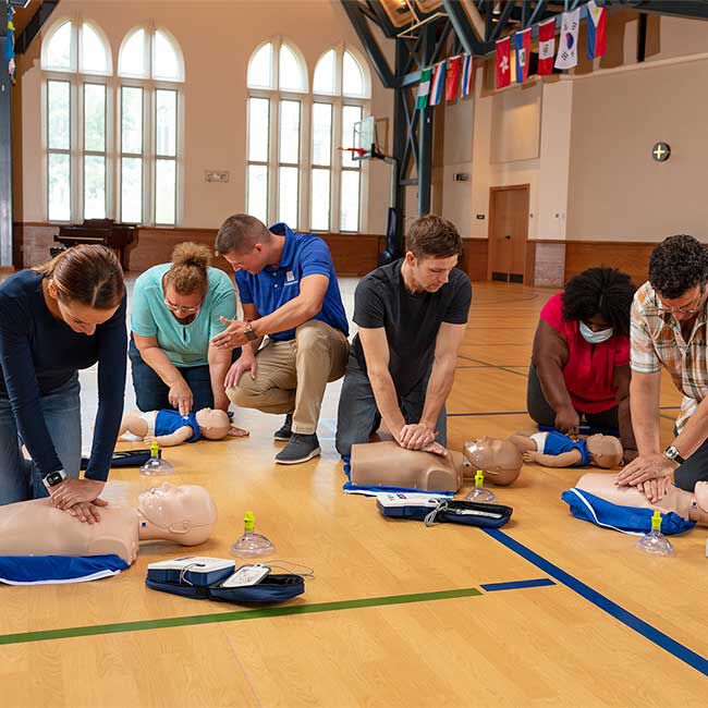 A group of students practicing chest compressions and using Prestan AED trainers on CPR manikins.