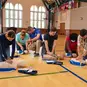 A group of students practicing chest compressions and using Prestan AED trainers on CPR manikins.
