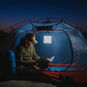 The LuminAID Max QI Lantern illuminated and hung up in a camping tent with a person reading a manual.