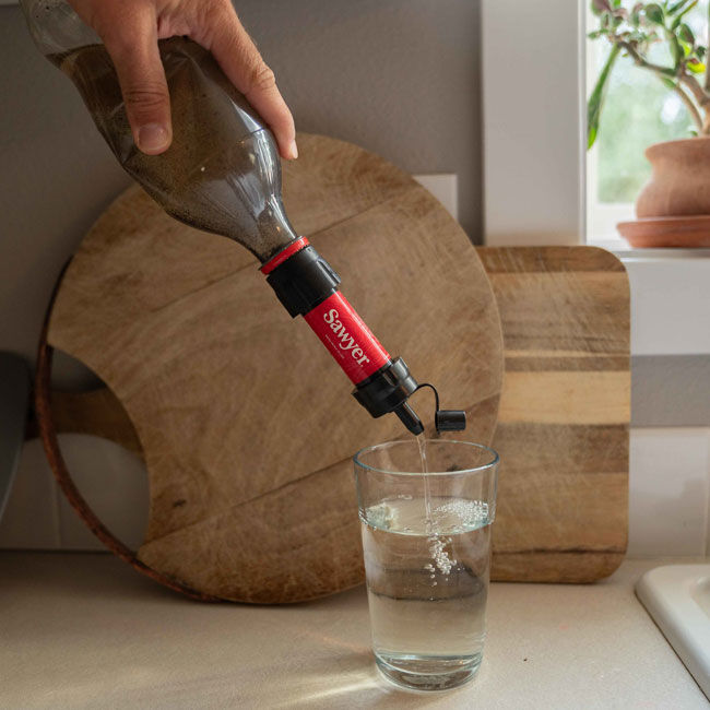 Sawyer Mini Water Filter attached to a bottle, filtering clean drinking water directly into a glass.