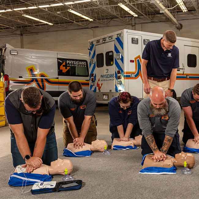 EMS students practicing CPR compressions with Adult Prestan Ultralite Manikins with instructor guidance.