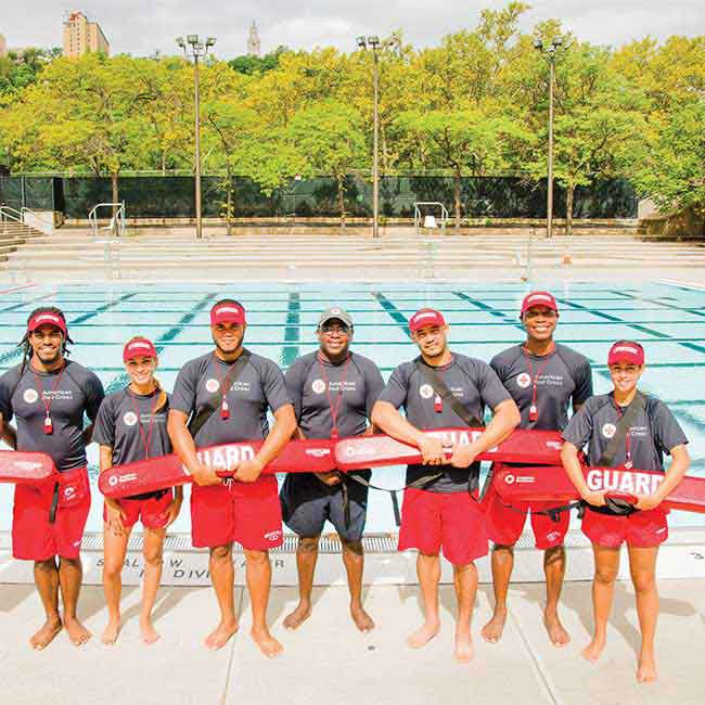 A group of lifeguards standing in front of a swimming pool holding rescue tubes.
