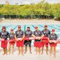 A group of lifeguards standing in front of a swimming pool holding rescue tubes.