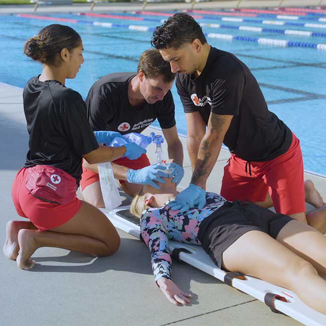 Three lifeguards performing CPR and performing rescue breaths with a bag valve mask.