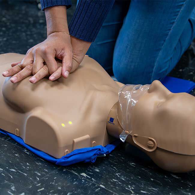 Student practicing CPR compressions on a Prestan Female Adult Manikin.