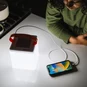 The LuminAID Max QI Lantern illuminated and charging a smartphone.