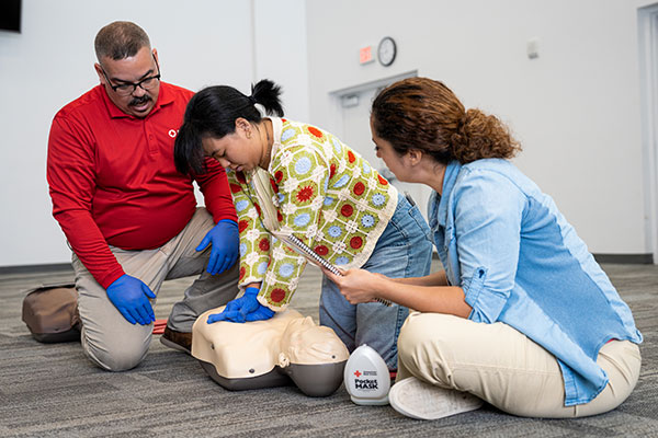 A woman practices performing CPR in Kentucky while another student watches and the instructor monitors.