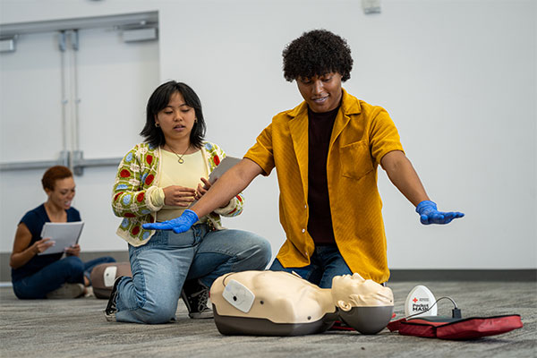 A student practices using an AED on a manikin in Rochester, New York demonstrating the clear step with arms spread.