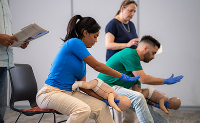 Students practicing back blows on infant CPR manikins with an instructor overseeing technique.